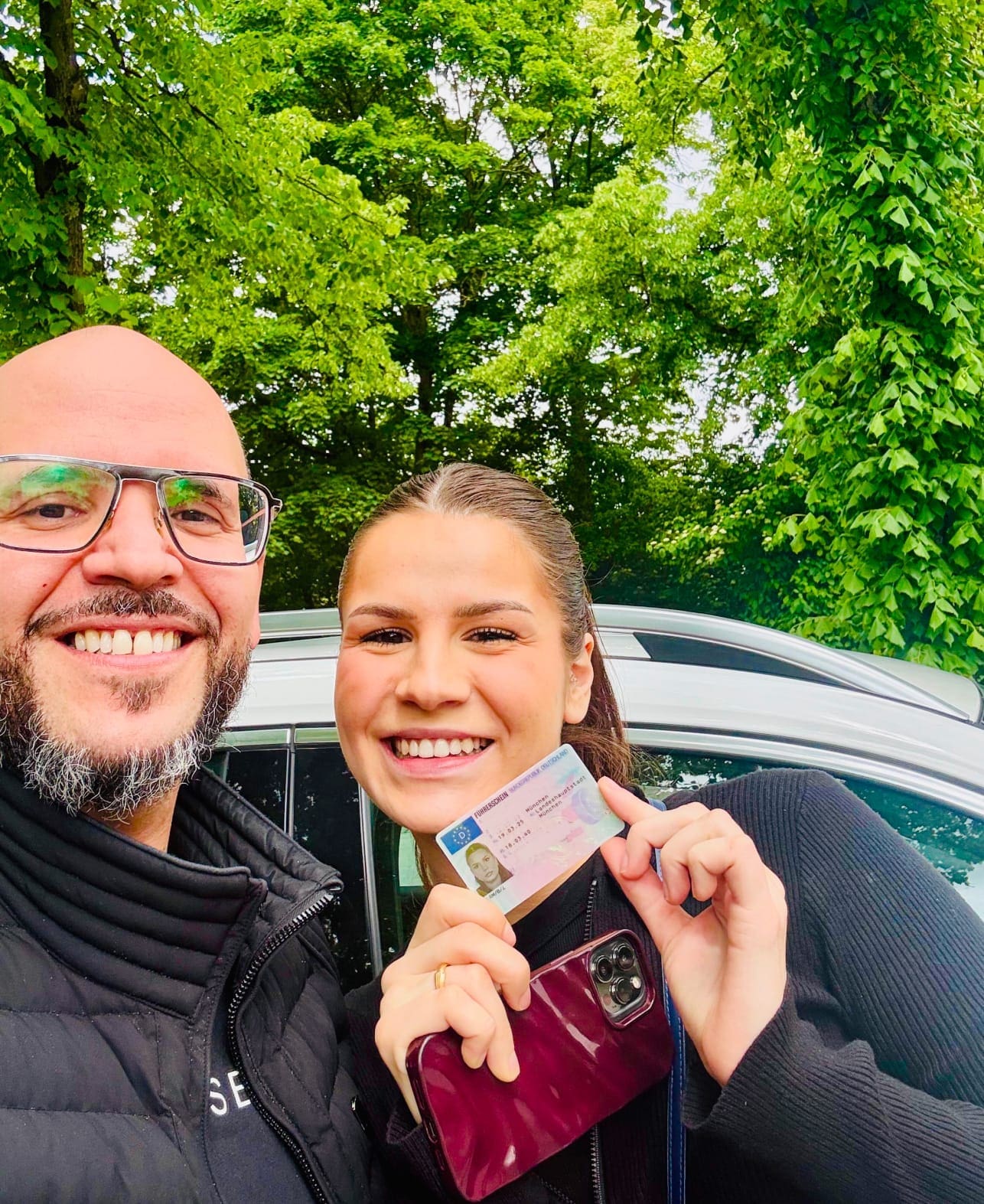 Driving instructor Zoran Janjic congratulates his student on passing her driving test—a happy moment in front of the driving school car in Munich.