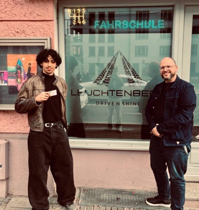 Fahrschüler mit frisch bestandenem Führerschein und Fahrlehrer Zoran Janjic vor dem Schaufenster der Fahrschule Leuchtenberg in der Einsteinstraße 131 in München.